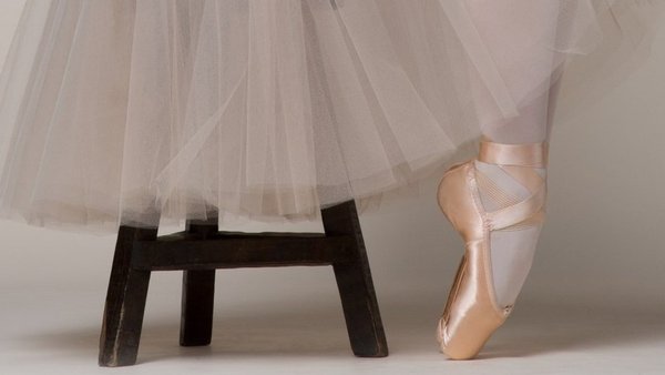 Füße einer Ballerina mit Tutu und Spitzenschuhe sitzend auf einem Stuhl